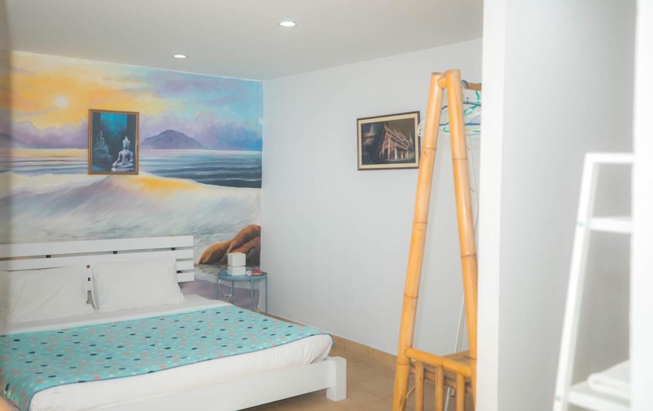 A bedroom with a bed, a painting of a Buddha on a wall, a ladder, and a framed picture.
