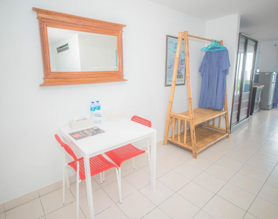 Een kamer met een witte tafel, rode stoelen, een houten bank, een spiegel en een deur.