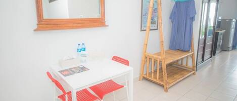 Een kamer met een witte tafel, rode stoelen, een houten bank, een spiegel en een deur.