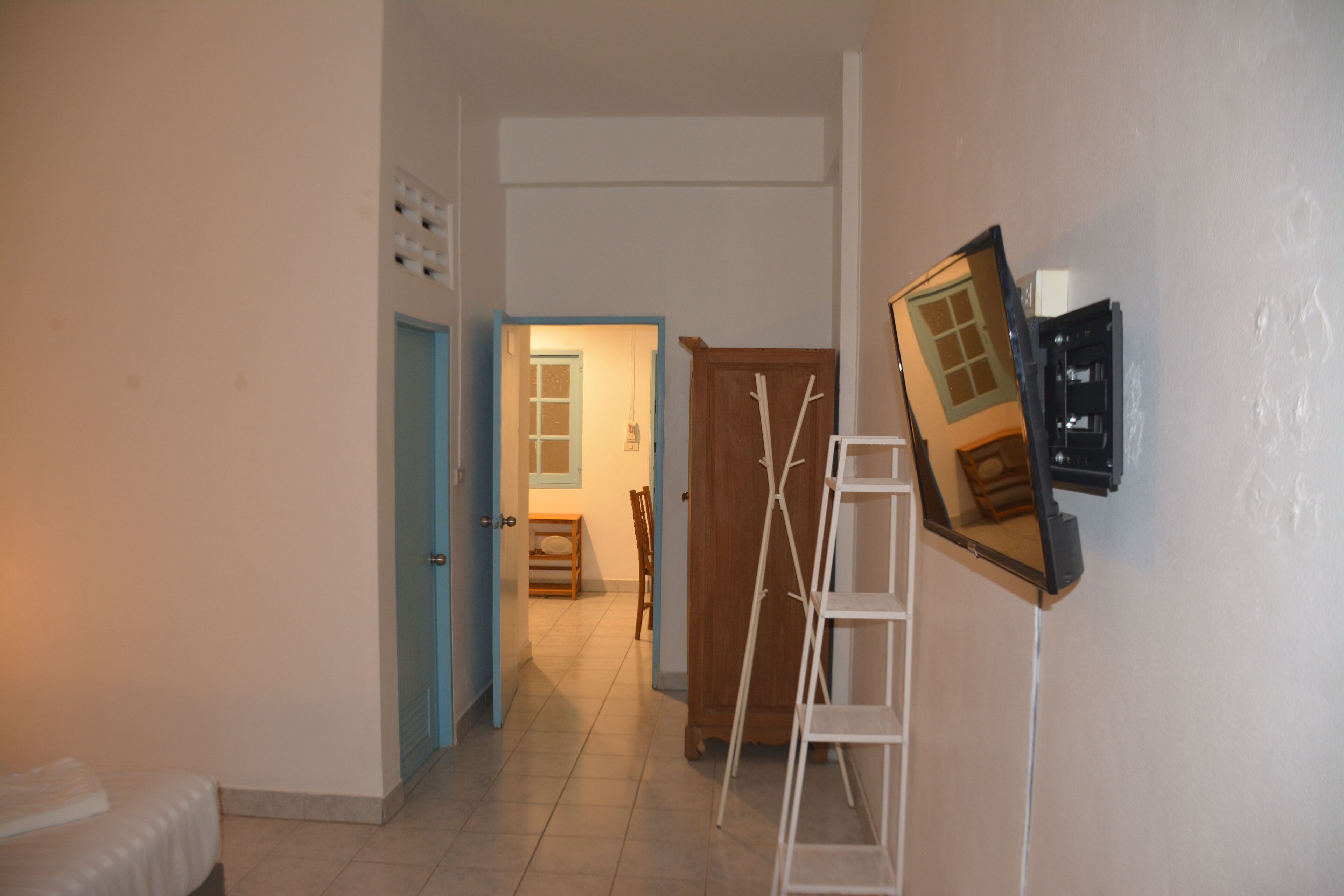 A hallway with a bed, a wooden wardrobe, and a ladder leaning against the wall.