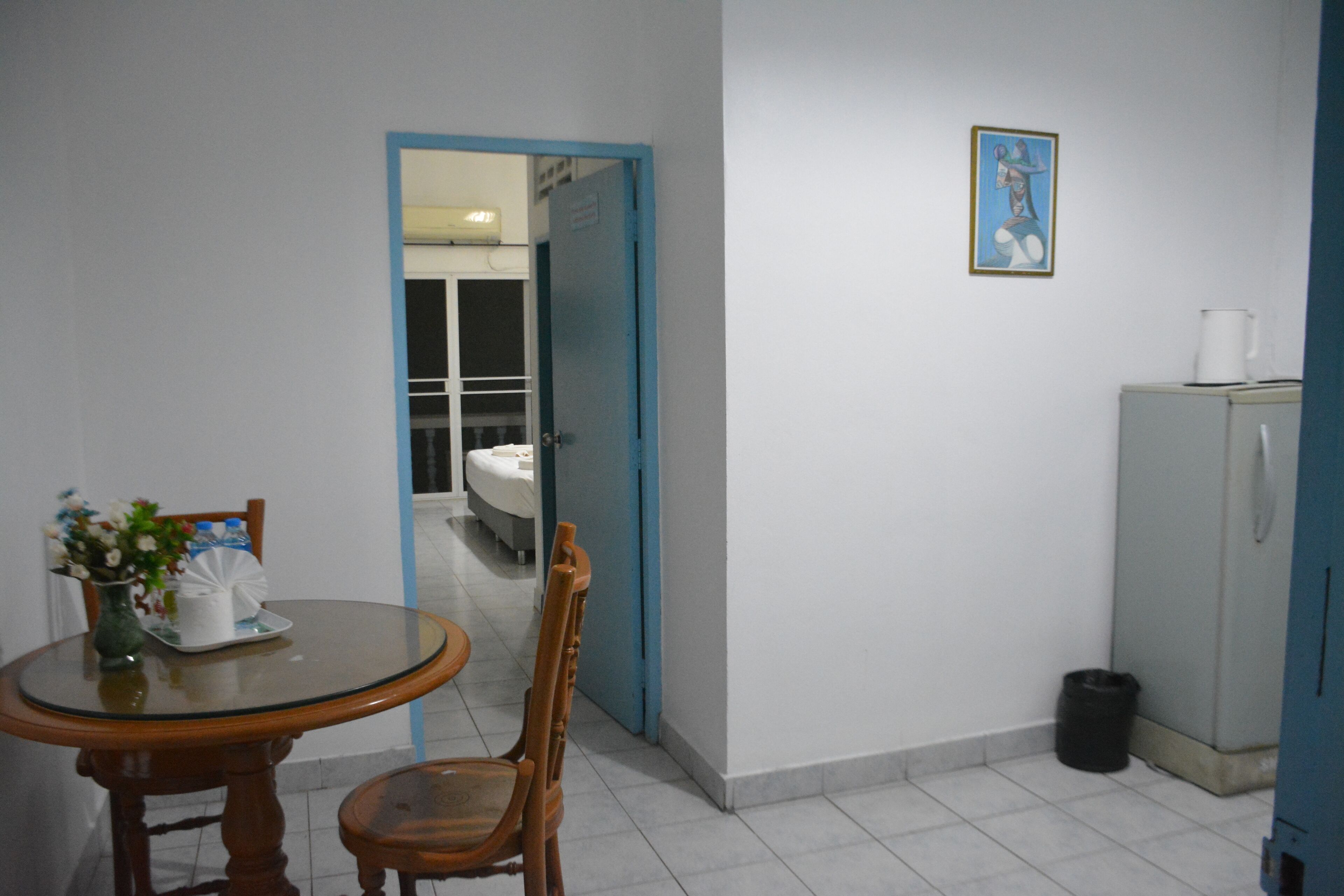 Un área de comedor con una mesa redonda, sillas, un florero con flores, un mueble aparador y una puerta que da a otra habitación.