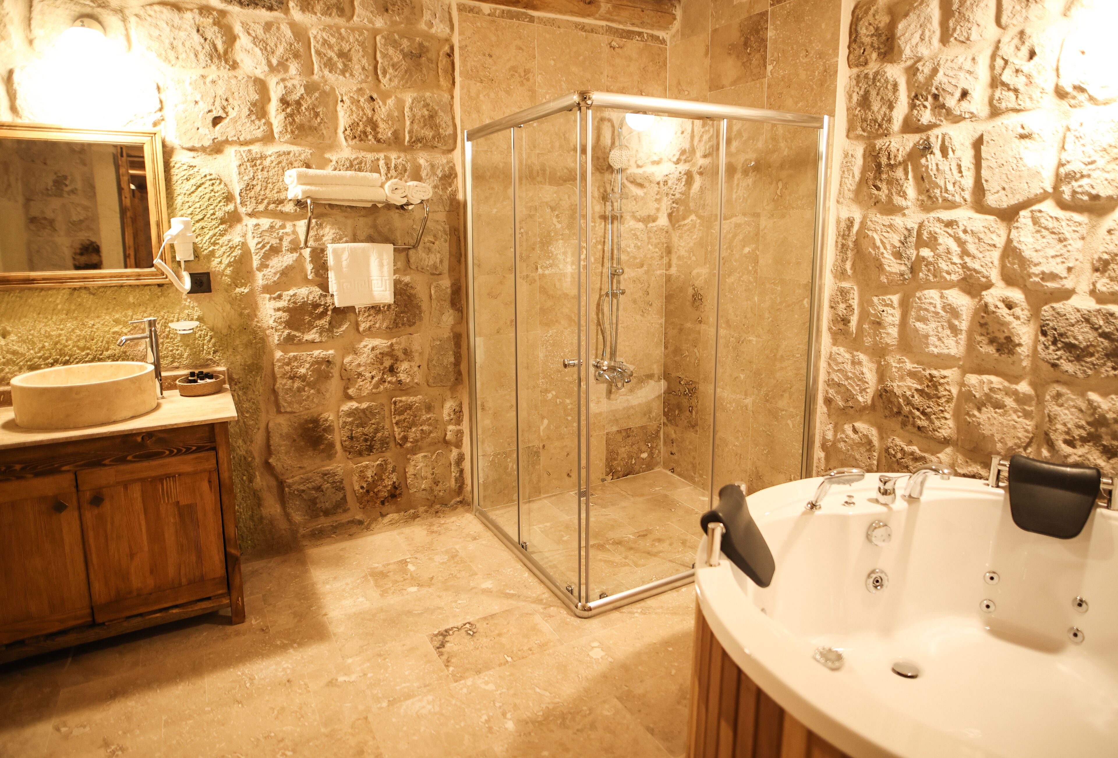 A bathroom with a stone wall, a glass shower enclosure, a wooden vanity with a sink, and a bathtub.