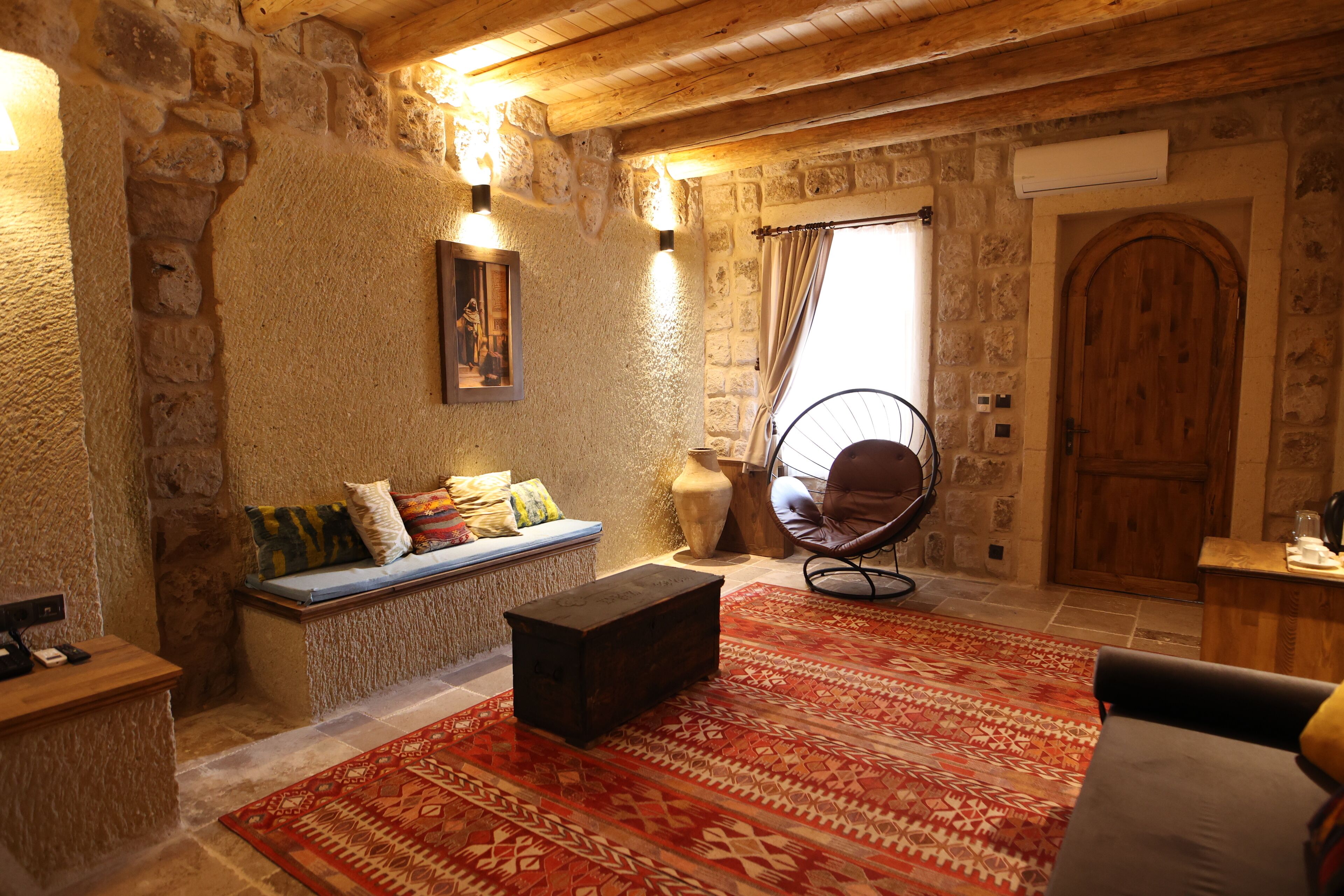 A rustic stone-walled room with a wooden bench, a rocking chair, and a patterned rug.