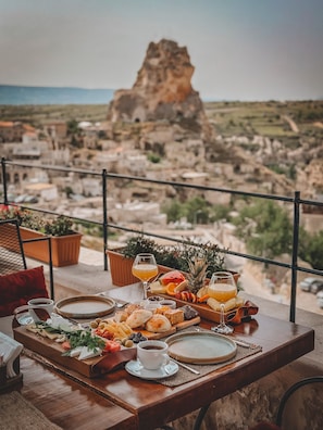 A dining table with a variety of food and drinks, overlooking a scenic landscape with a prominent rock formation.
