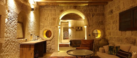 A stone-walled room with a wooden ceiling, a round table, a sofa, and a small bar area.