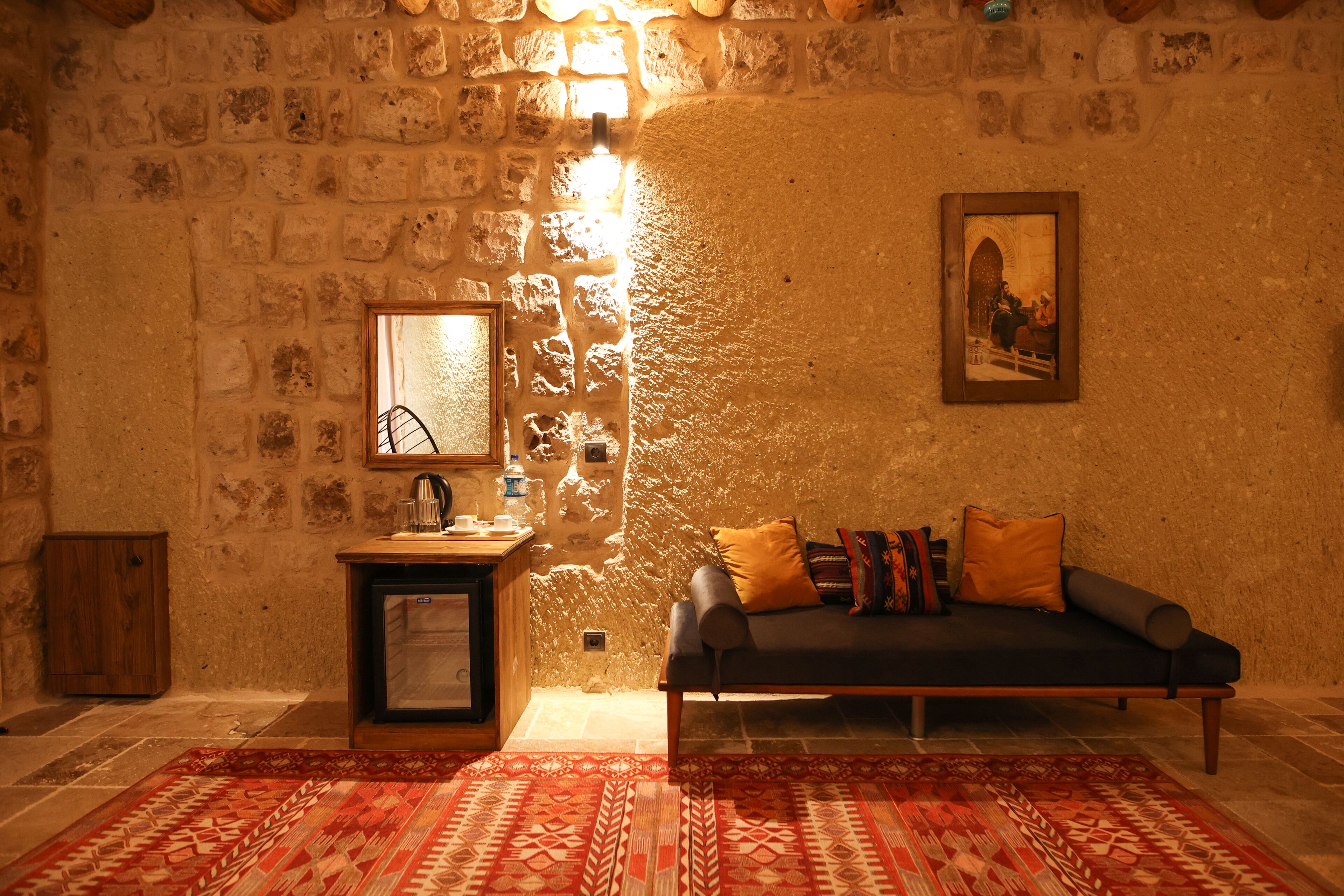 A cozy room with a stone wall, a wooden cabinet, a sofa with cushions, a patterned rug, and a framed picture on the wall.