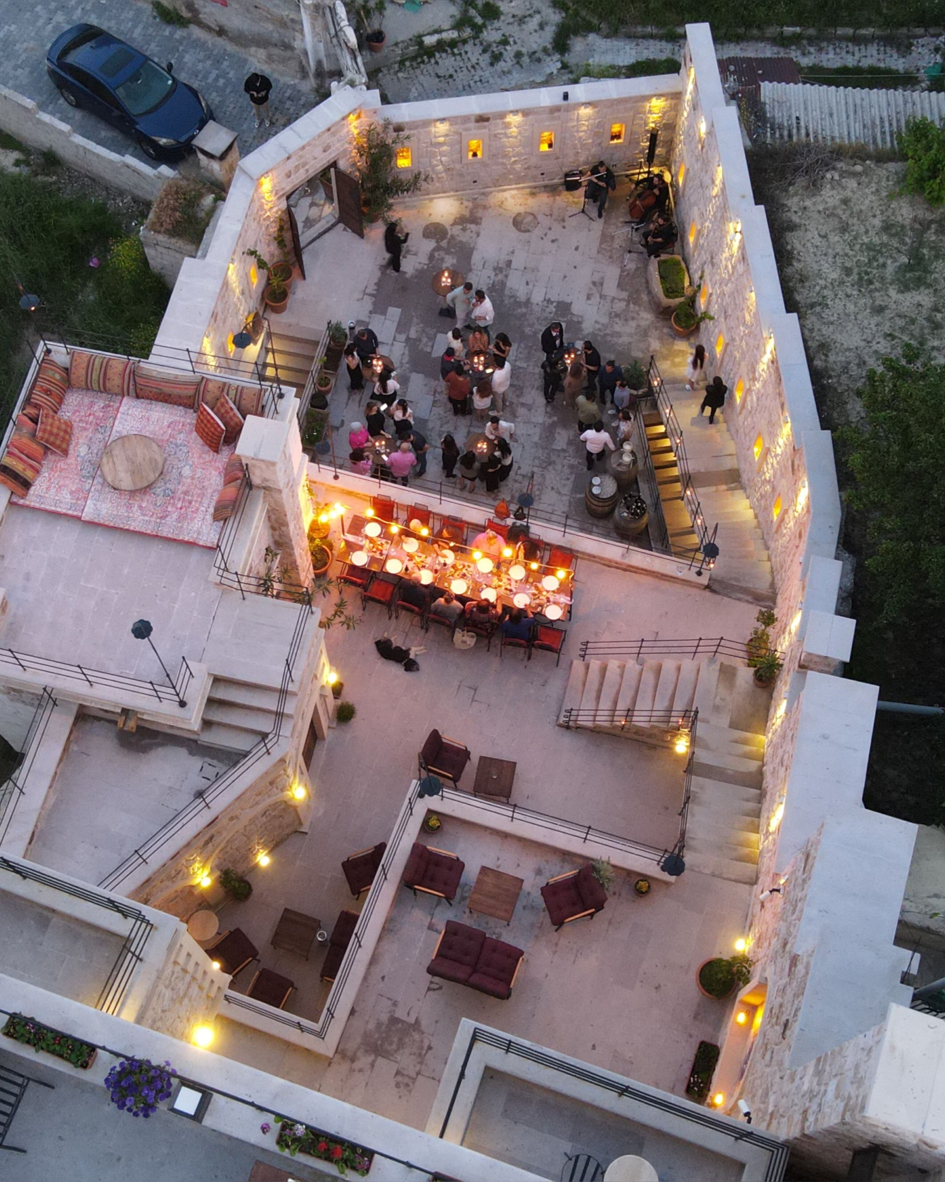 An outdoor patio area with multiple seating arrangements, including round tables and sofas, surrounded by stone walls and potted plants.