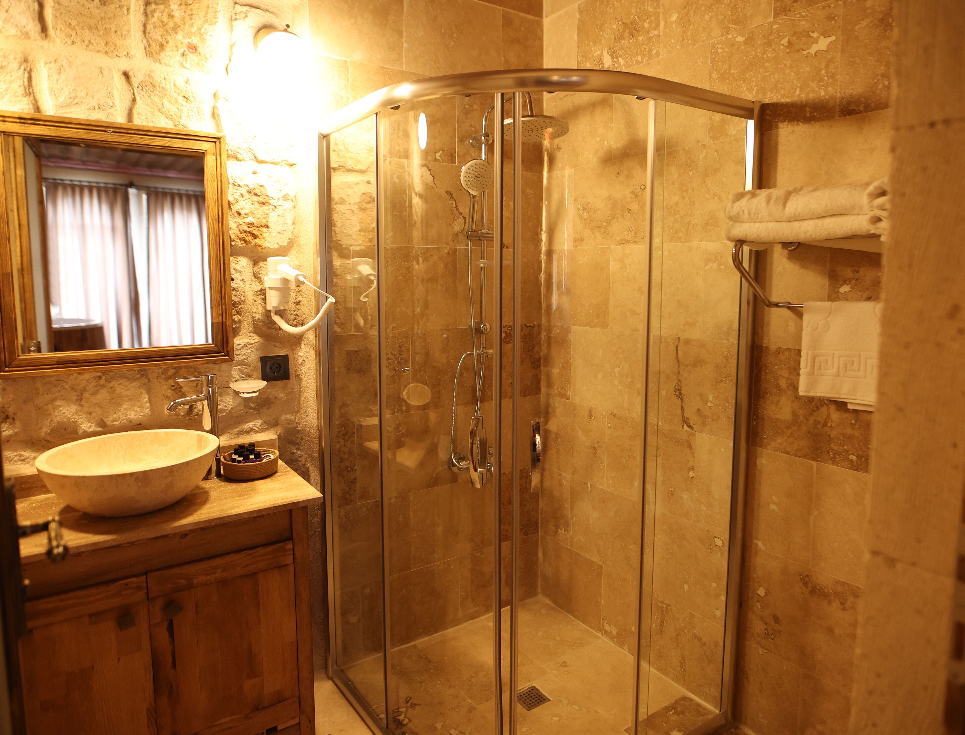 Una ducha con cerramiento de vidrio y puerta curva, un tocador de madera con lavabo y un espejo sobre el lavabo.