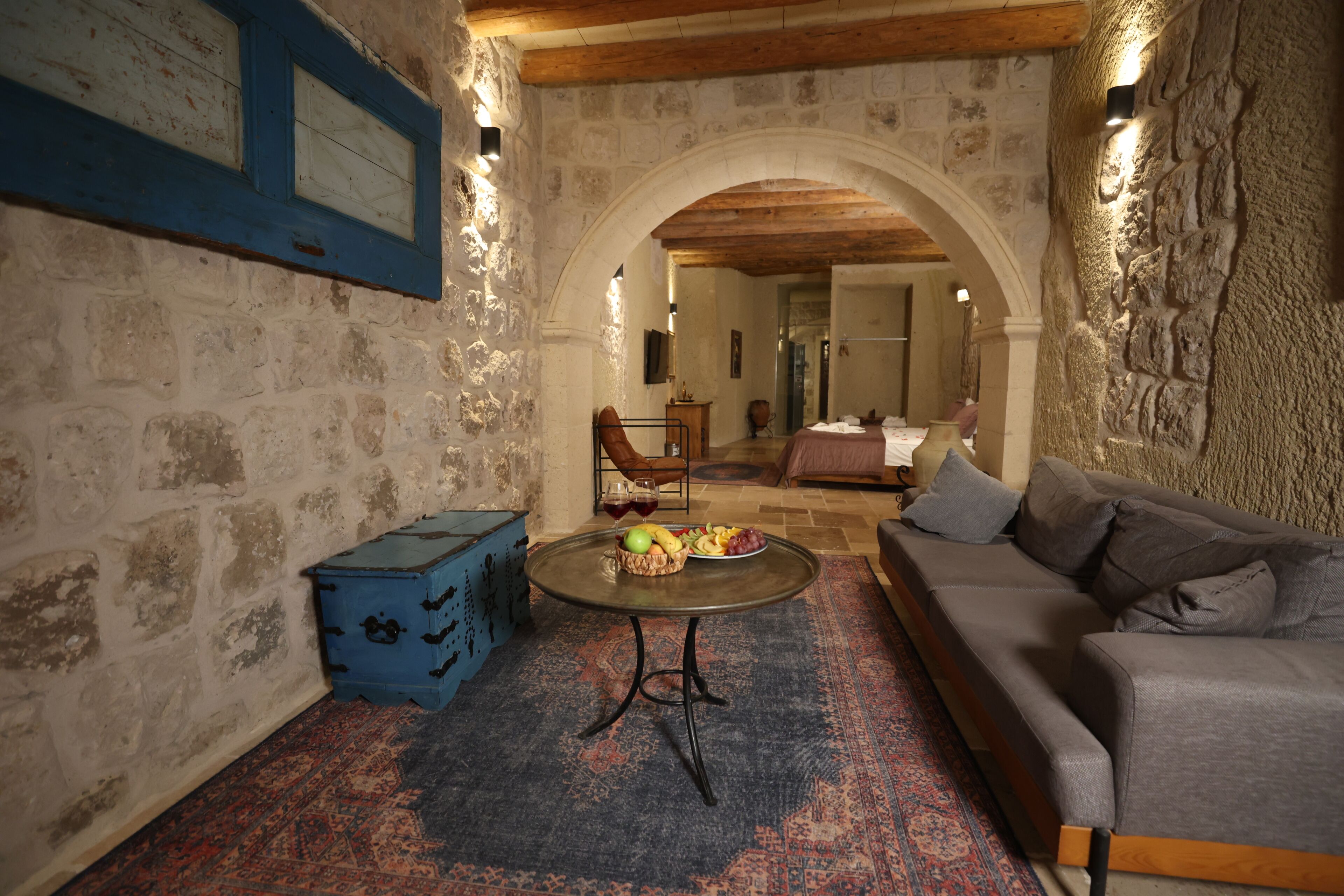 A stone-walled room with a sofa, a table with fruit, and a blue chest of drawers.