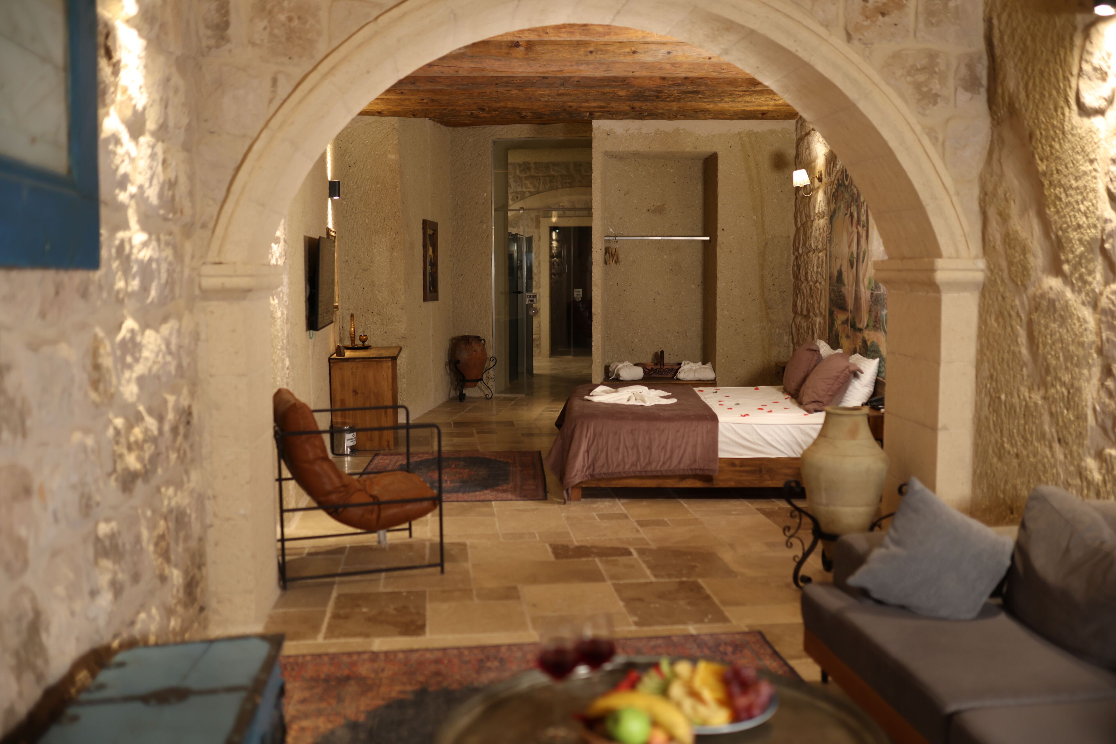 A room with a bed, a chair, a sofa, a vase, and a fruit bowl.