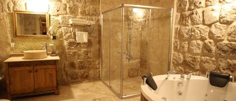 A bathroom with a stone wall, a wooden vanity, a glass-enclosed shower, and a freestanding bathtub.