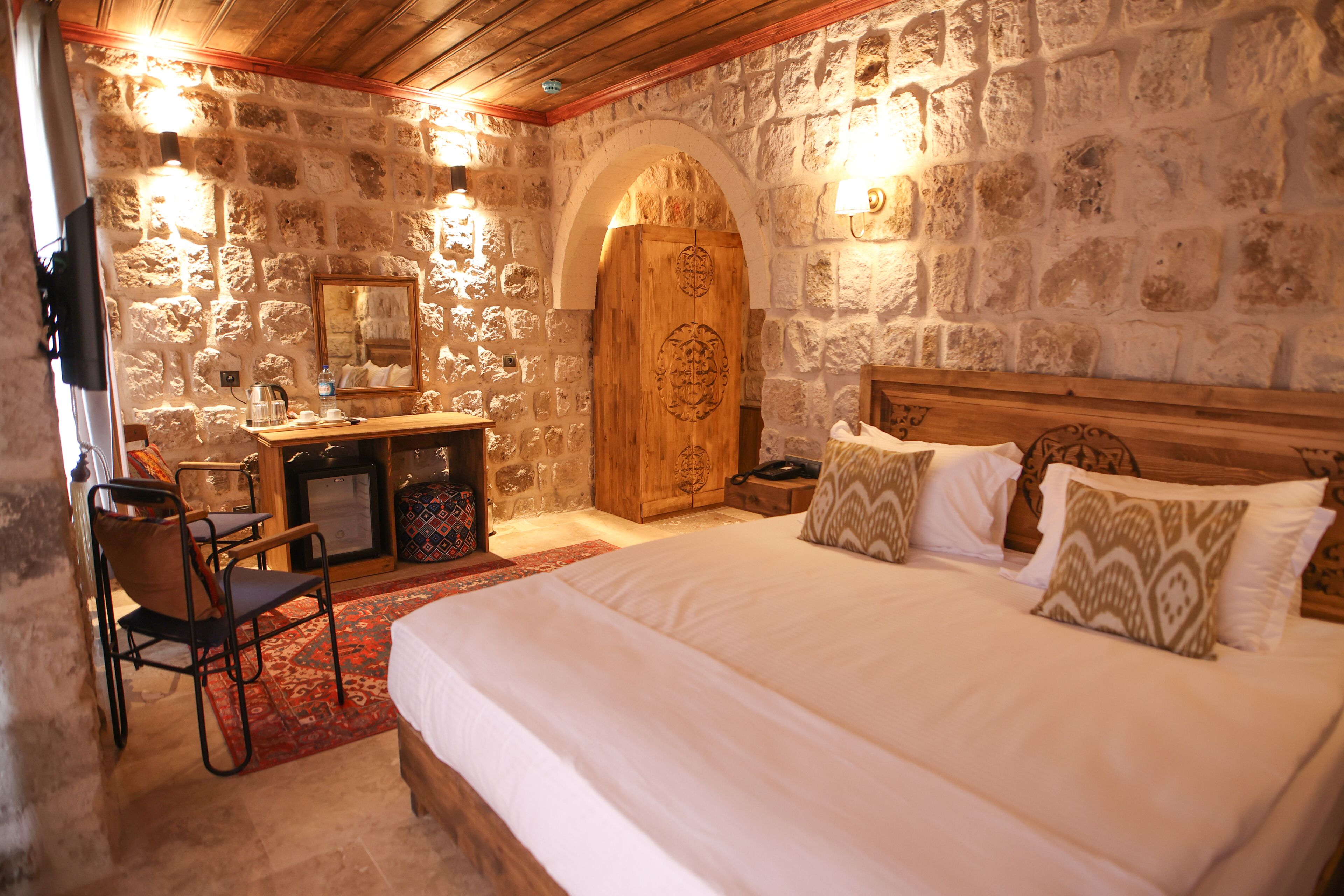 Dormitorio con paredes de piedra, una cama, un escritorio y un espejo.