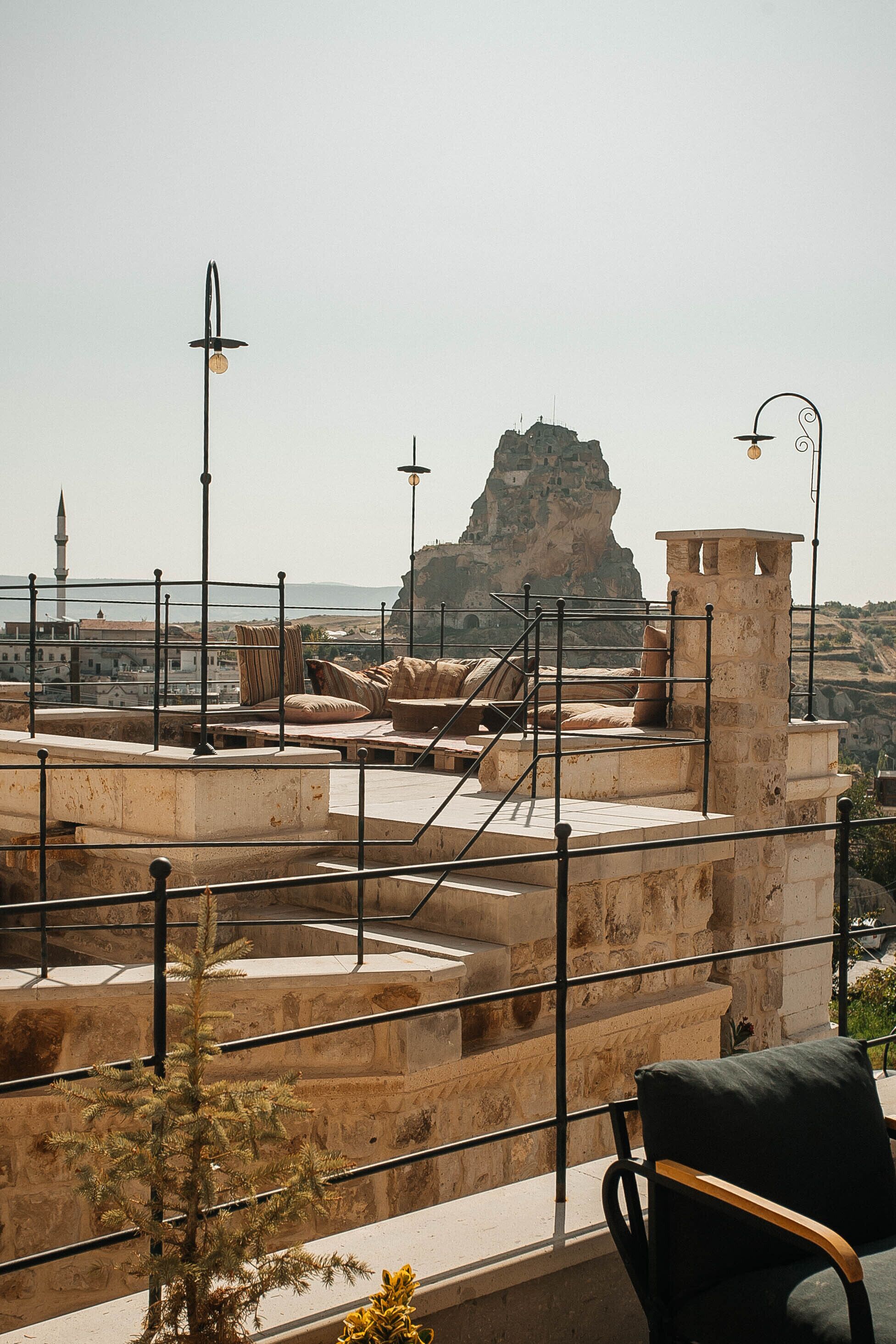 A rooftop terrace with stone railings, a chair, and a view of a mountain and a mosque.