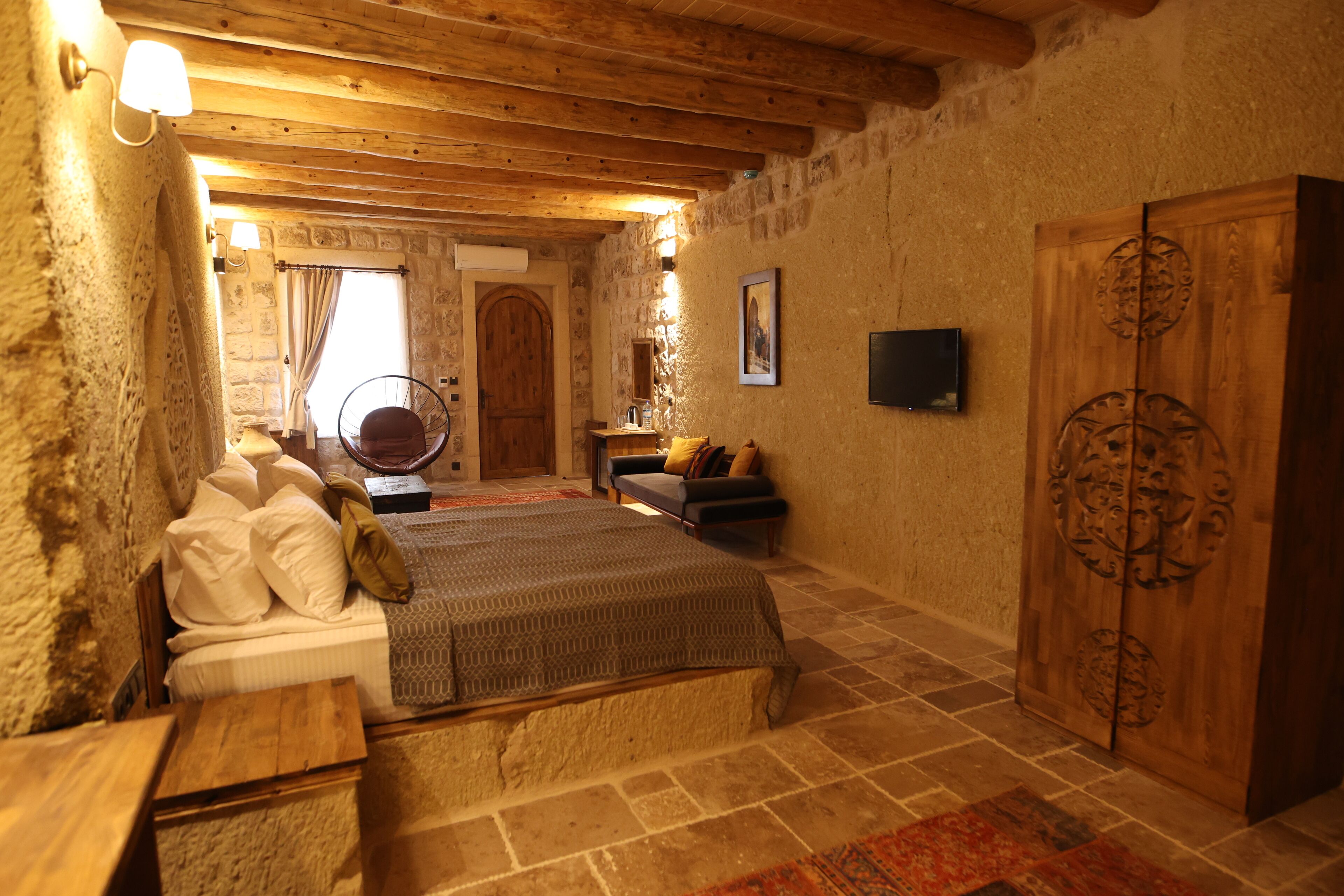 A rustic bedroom with a wooden bed, a wooden wardrobe, and a stone wall.
