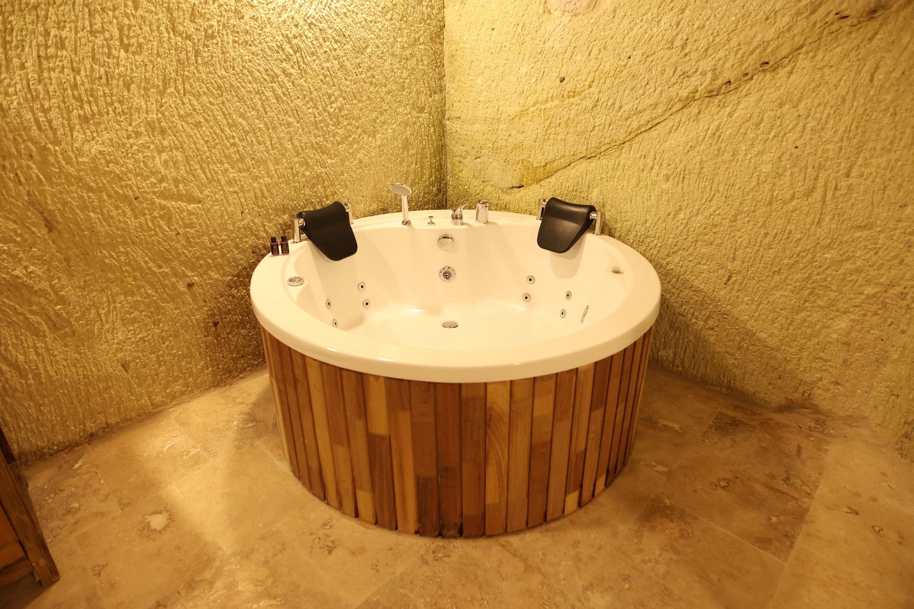 Una bañera de madera circular con dos asientos negros, frente a paredes con textura.