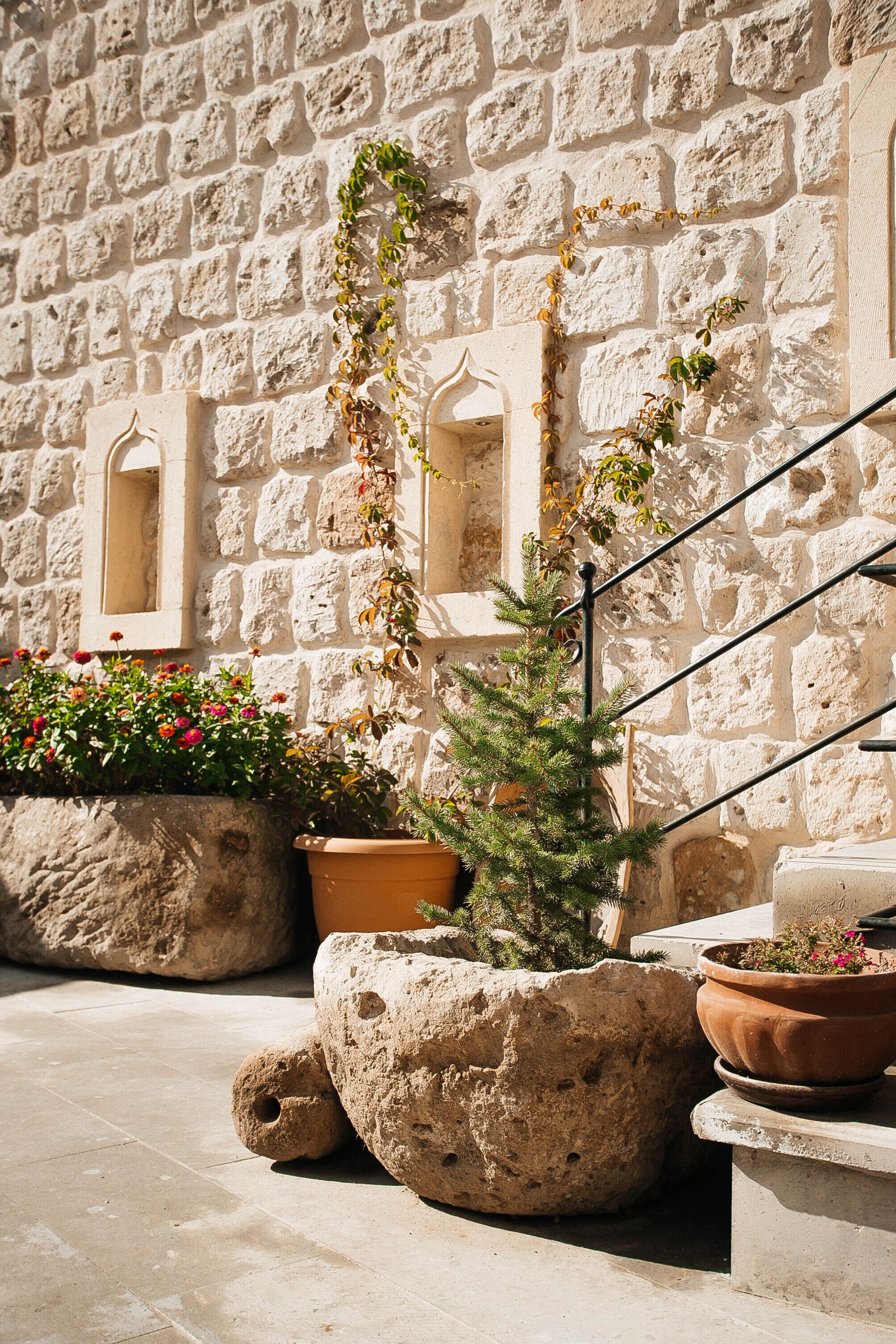 A stone wall with a window, potted plants, and a staircase.
