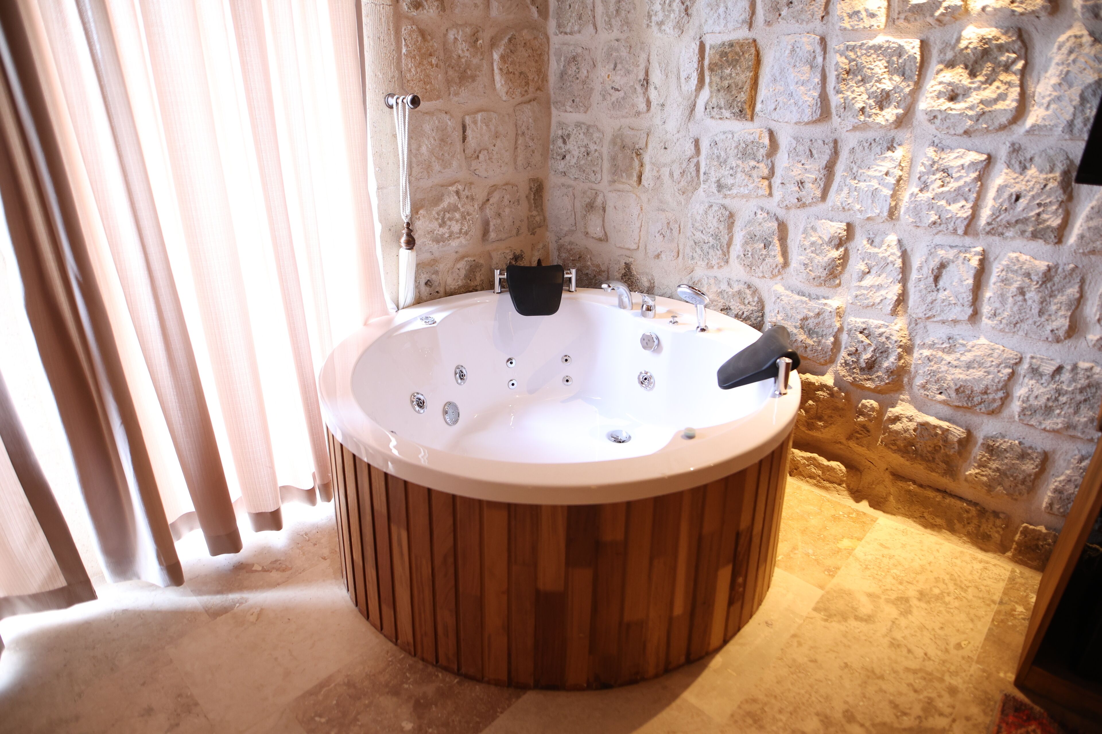 Una bañera de madera en un baño con paredes de piedra y zona de ducha.