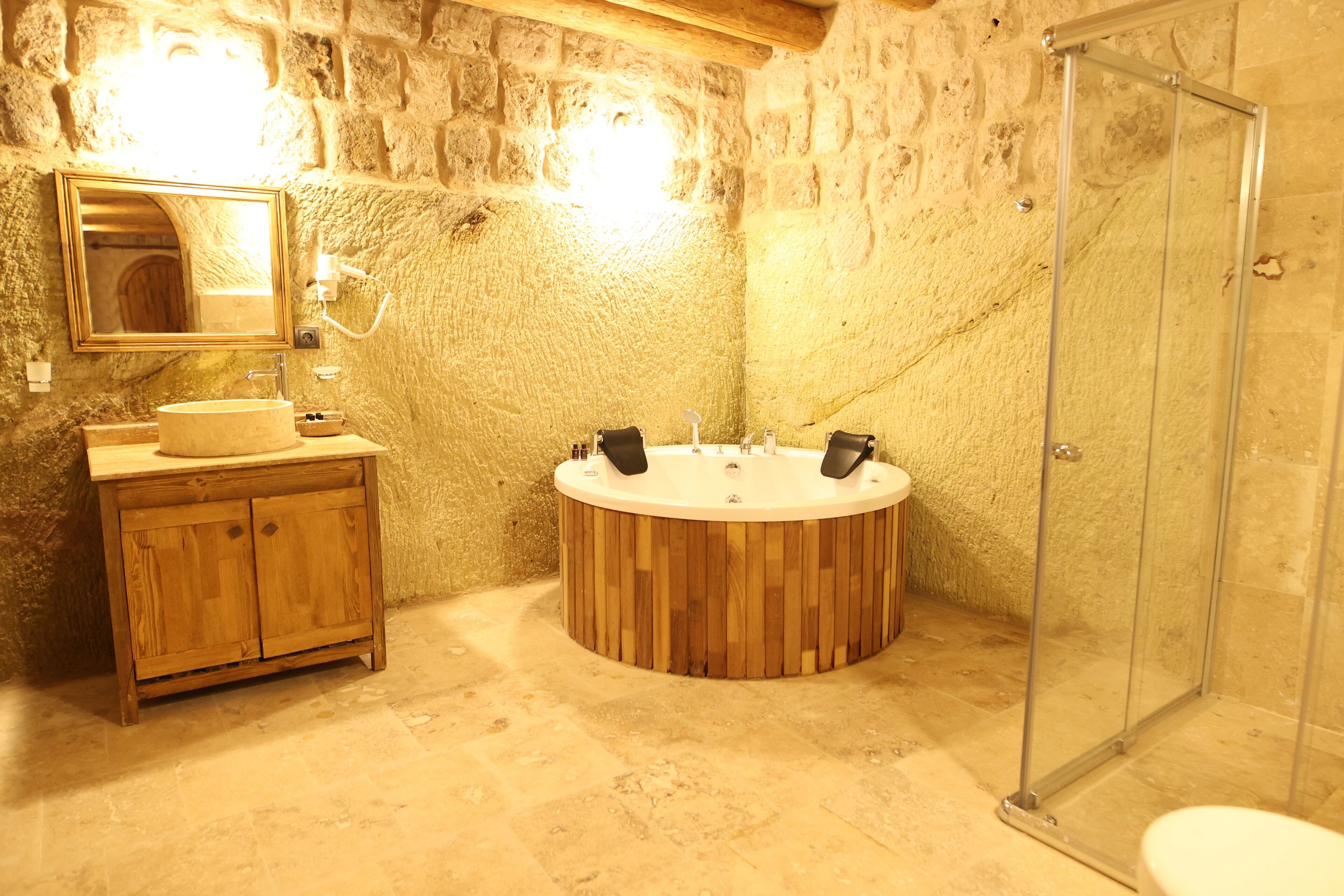 Ein Badezimmer mit Steinwänden, einem Holzausziehtisch, einer freistehenden Badewanne und einer Duschkabine aus Glas.