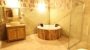 Ein Badezimmer mit Steinwänden, einem Holzausziehtisch, einer freistehenden Badewanne und einer Duschkabine aus Glas.