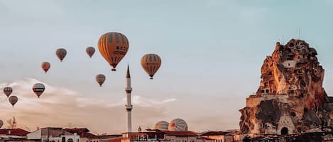Uma cidade histórica com arquitetura tradicional, um minarete imponente e balões de ar quente no céu.