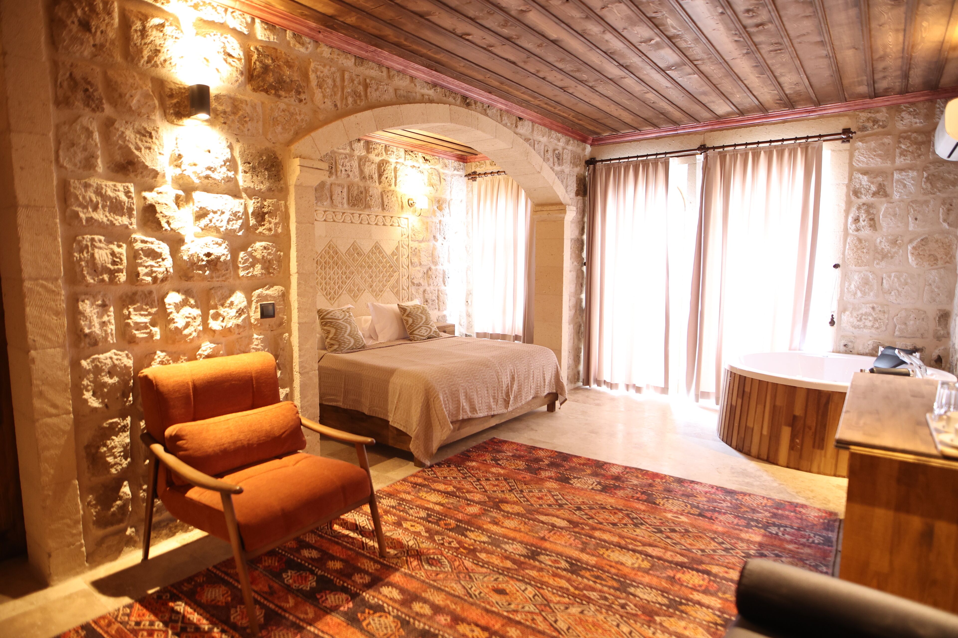 A bedroom with a stone wall, a bed, a chair, and a small bathroom area.