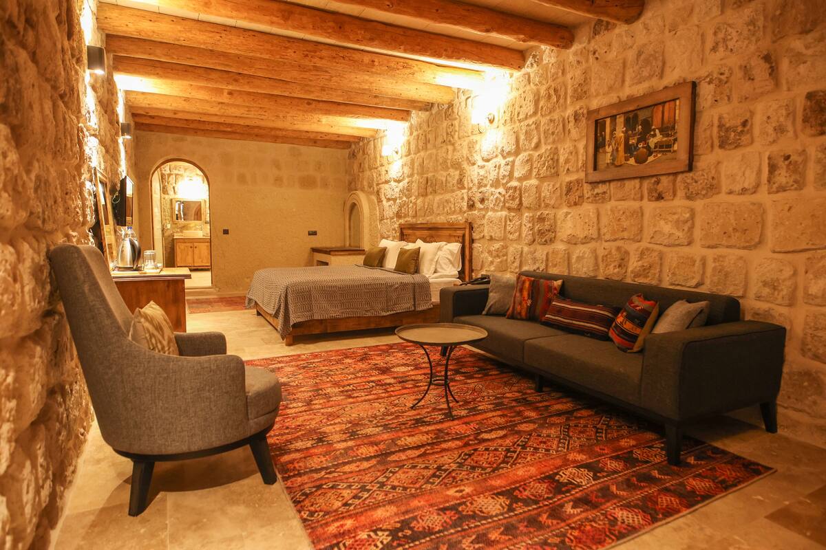 Habitación acogedora con cama, sofá, sillón y una mesita. Se observa una pared de piedra y un techo de madera.