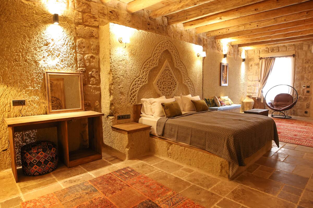 Un dormitorio rústico con paredes de piedra, una cama de madera, una mesita de noche, un espejo y una silla.