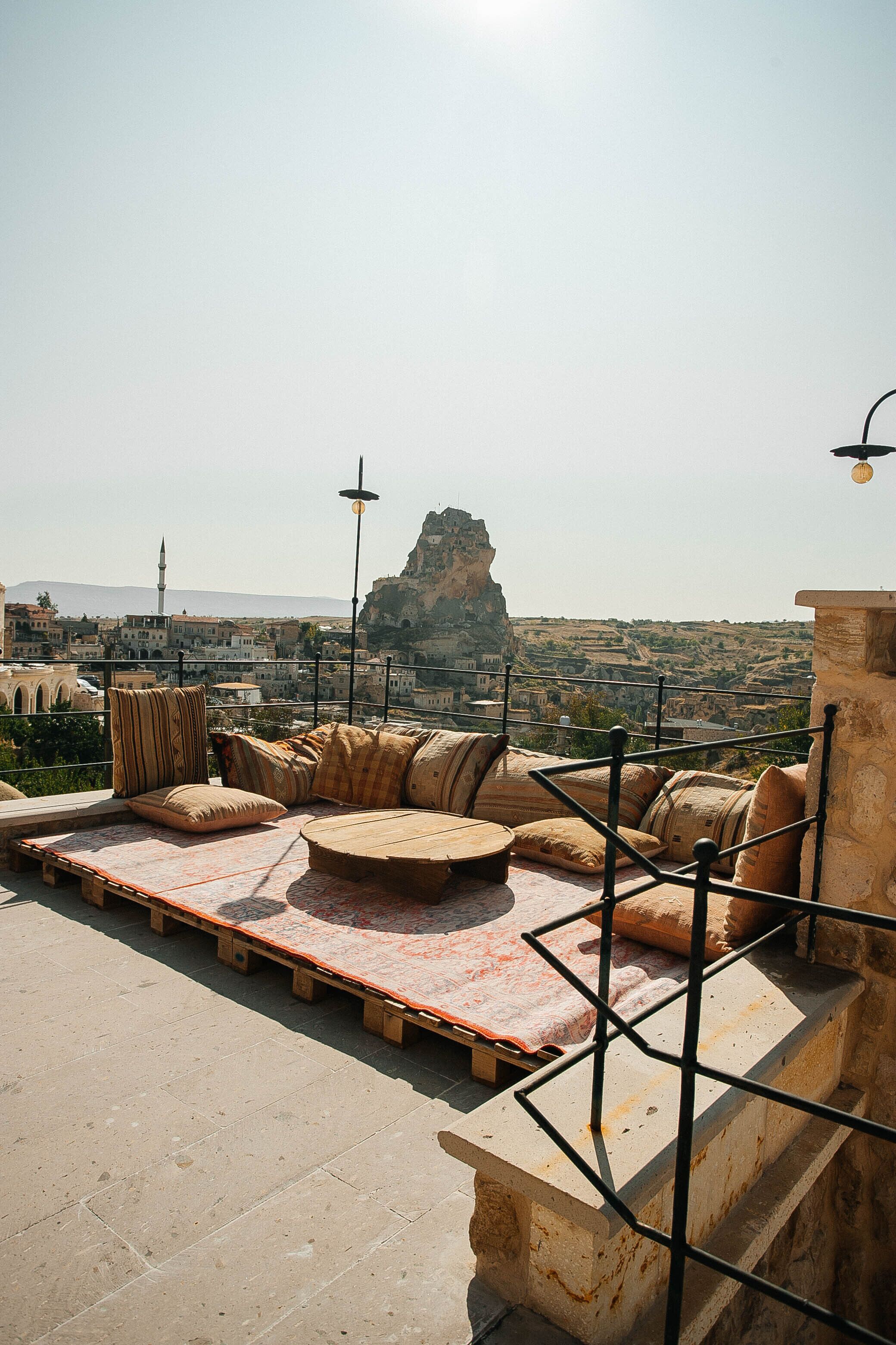 A rooftop terrace with a seating area, a view of the cityscape, and a prominent rock formation in the distance.