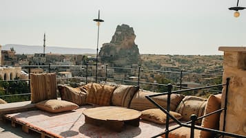 A rooftop terrace with a seating area, a view of the cityscape, and a prominent rock formation in the distance.