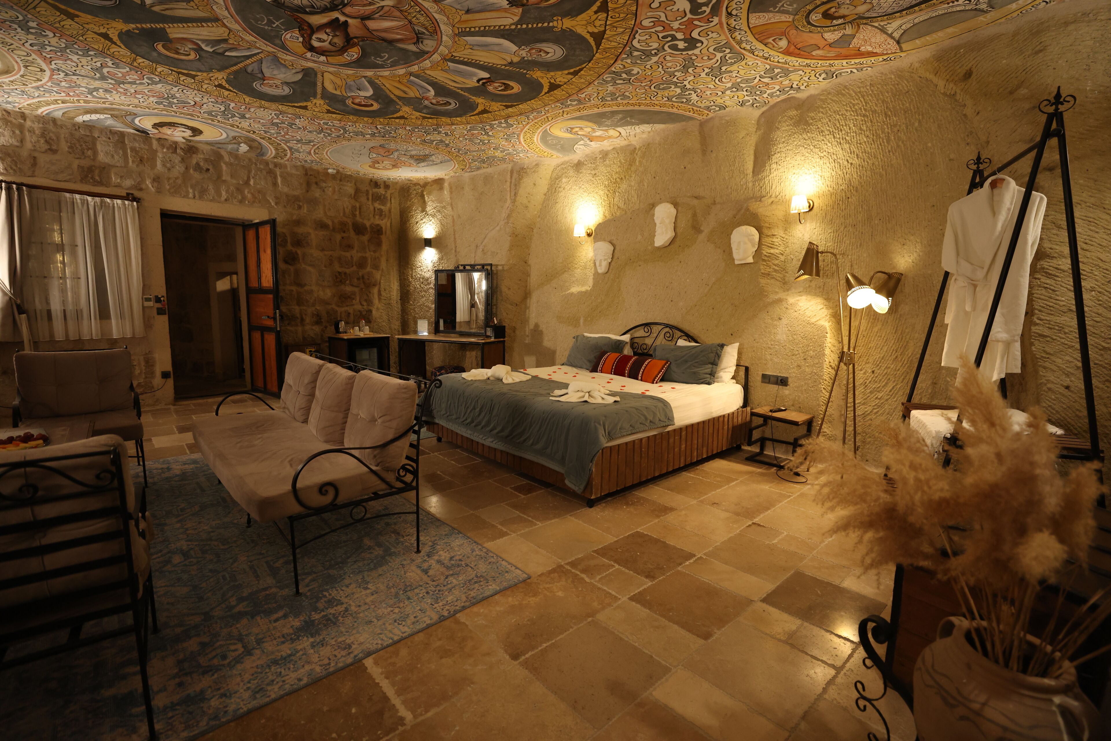A room with a bed, a sofa, a mirror, and a ceiling with intricate designs.