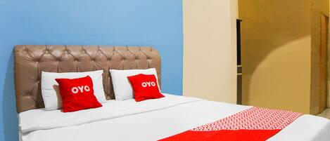 A bed with a tufted headboard, two pillows with 'OYO' branding, and a red and white patterned throw.
