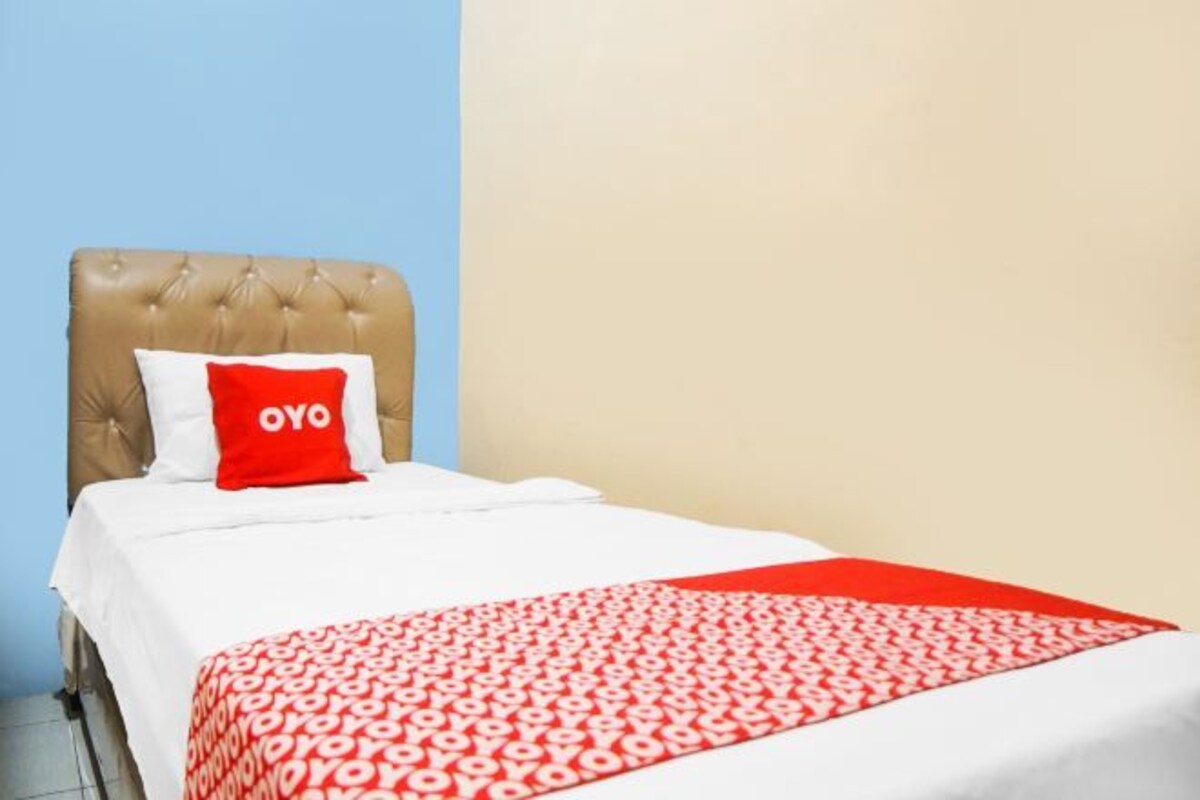 Una cama bien hecha con una colcha de rayas rojas y blancas y una almohada roja con la palabra 'OYO' escrita.