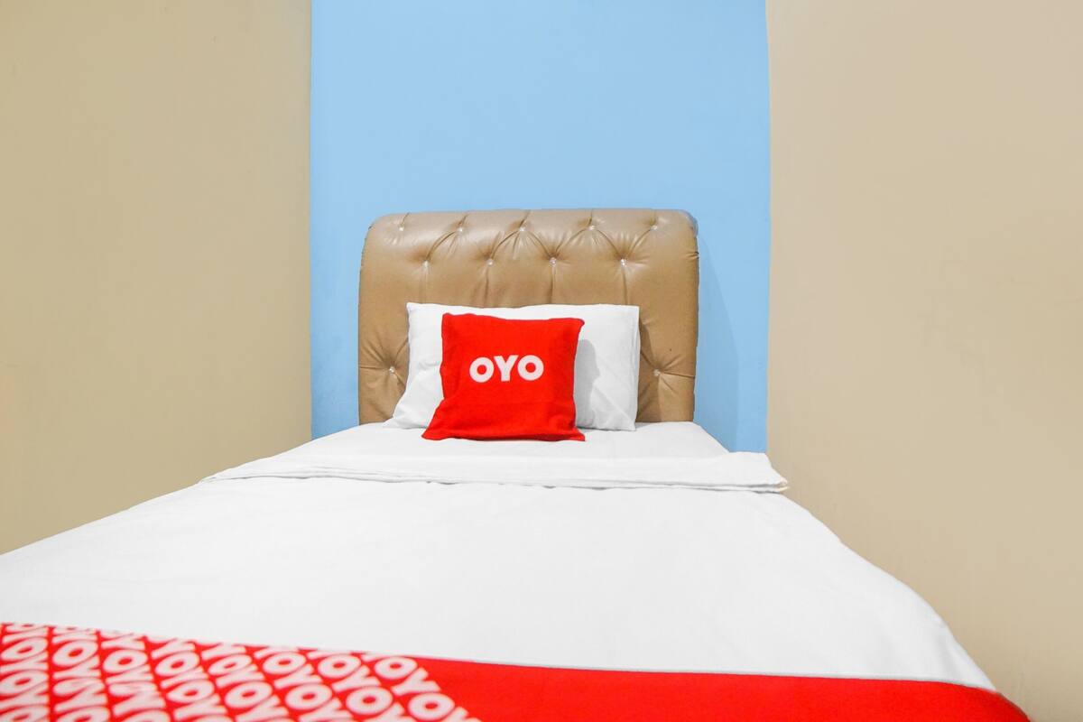 A bed with a white and red bedspread, a red pillow with "OYO" text, and a beige headboard against a blue wall.