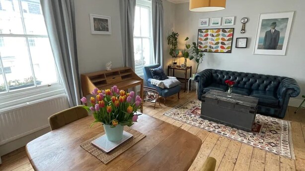 A living room with a wooden dining table, blue sofa, and a patterned rug. - Beautiful Vintage Style 1BD Apartment - Pimlico (London)