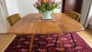 A dining table with a floral centerpiece, surrounded by chairs, on a patterned rug. - Beautiful Vintage Style 1BD Apartment - Pimlico (London)