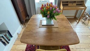A dining table with a vase of tulips, a wooden side table, a patterned rug, and a bookshelf. - Beautiful Vintage Style 1BD Apartment - Pimlico (London)