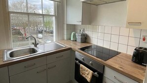A kitchen with a window, stainless steel sink, black stove, and white cabinets. - Beautiful Vintage Style 1BD Apartment - Pimlico (London)