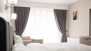 Una habitación de hotel con una cama grande, una silla, un escritorio y un ventanal con cortinas.