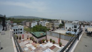 A rooftop terrace with potted plants, a patterned floor, and a view of surrounding buildings and hills. - SJH Venkatesh (Haridwar)