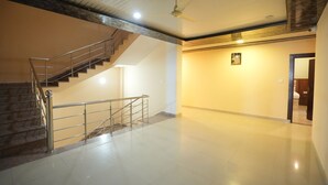 A spacious interior with a staircase, a ceiling fan, and a plain wall with a small picture. - SJH Venkatesh (Haridwar)