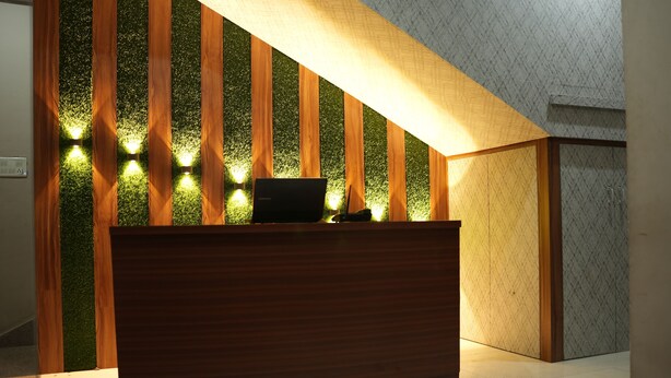 A reception desk with a laptop, surrounded by vertical wooden panels with green foliage and lights. - SJH Venkatesh (Haridwar)
