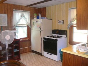 Compact kitchen with a functional layout, featuring a refrigerator, gas stove, and fan.