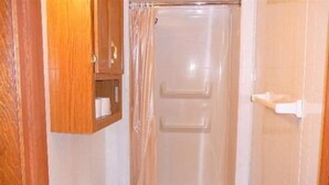 Ein kleines Badezimmer mit Dusche, Toilette und einem Holzschrank.