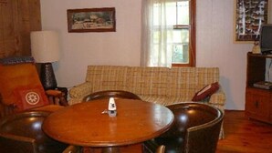 Ein Wohnzimmer mit einem grauen Sofabezug, einem Holztisch und einem Fernseher auf einer Holzkommode.