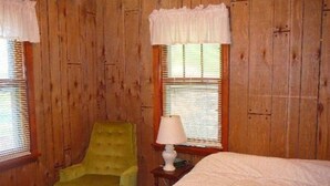 Ein Zimmer mit Holzwandverkleidung, einem grünen Sessel, einem Nachttisch mit Lampe und einem Bett mit weißer Bettdecke.