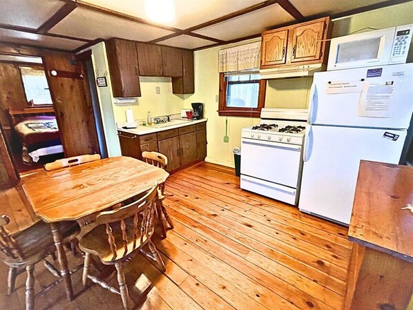Cocina compacta con suelo de madera, una mesa de comedor y electrodomésticos básicos, como estufa, microondas y refrigerador.