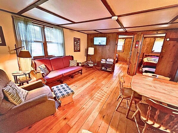 A cozy living room with a red sofa, a wooden dining table, and a fireplace. - Thunderhead Lodge ~ Cabin 3 (Butternut)