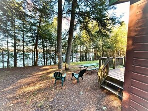Un área de picnic con dos sillas Adirondack y una mesa, rodeada de árboles y una terraza de madera.