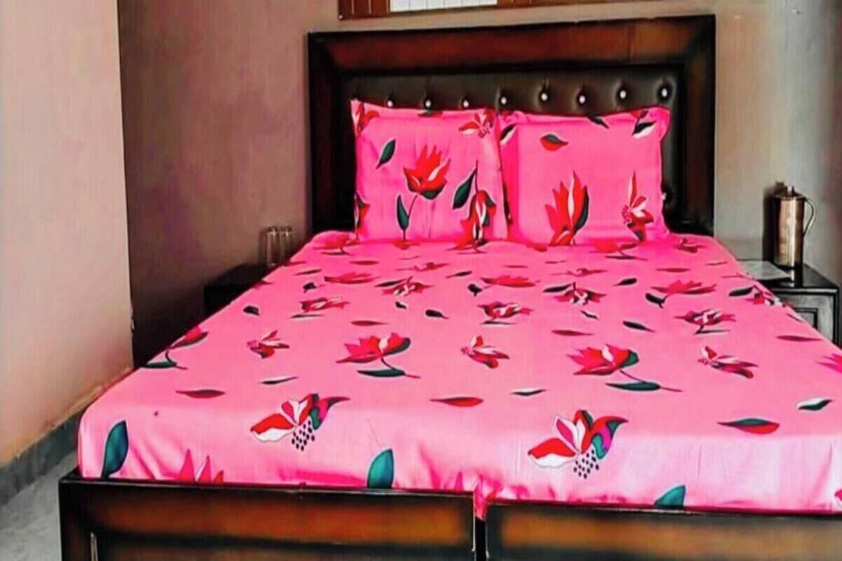 A bed with a floral bedspread and matching pillows, a wooden headboard, and a nightstand with a lamp.