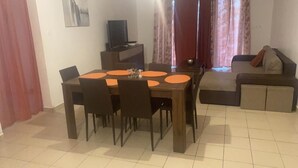 A dining area with a wooden table and chairs, a television on a stand, and a sofa in the background. - Spacious apartment with pool and gorgeous views of Marigot! (Marigot)